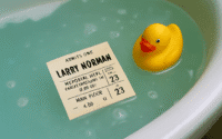 Yellow rubber duck floats beside a submerged event ticket in blue-green bathwater.